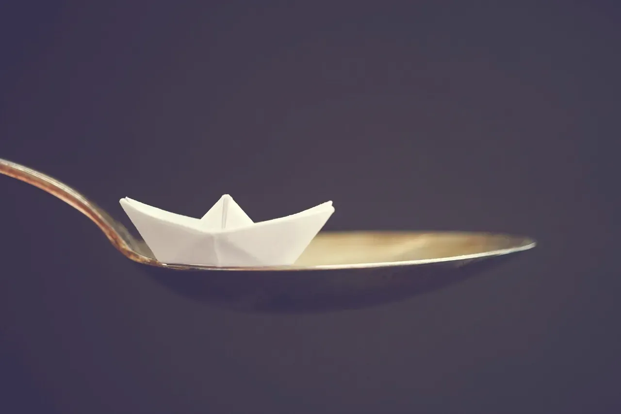 A folded paper boat resting in the bowl of a spoon